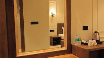 A hotel room with a large mirror, wooden bench, bedside table, and a small kitchenette area.