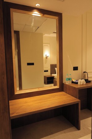 A hotel room with a large mirror, wooden bench, bedside table, and a small kitchenette area.