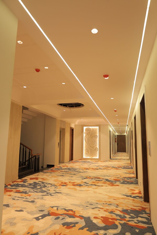 A hotel corridor with a patterned carpet, recessed lighting, and a decorative wall panel.