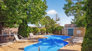 Une piscine entourée d’arbres et d’un petit bâtiment, avec des chaises longues à proximité.