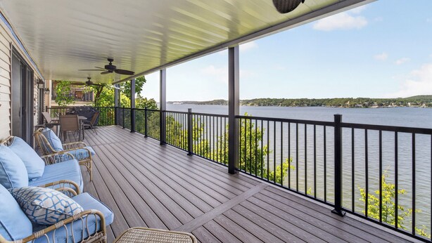 Une terrasse couverte, aménagée avec du mobilier d’extérieur, dotée d’une rambarde et offrant une vue sur un lac.