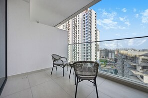 A balcony with two wicker chairs and a table, overlooking a cityscape with high-rise buildings. - Bloomfields Studio in NAS3 - Arjan  (Dubai)
