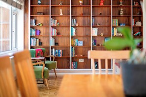 A room with a large wooden bookshelf filled with books and decorative items, a green armchair, and a wooden table. - Spacious Home near Addenbrookes with Free Parking - Pass the Keys (Cambridge)