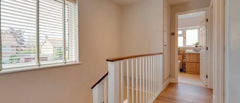 A hallway with a wooden floor, white railing, and a window with blinds.