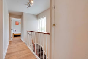 A hallway with a wooden floor, white walls, a staircase with a wooden railing, and a bed in the background. - Spacious Home near Addenbrookes with Free Parking - Pass the Keys (Cambridge)
