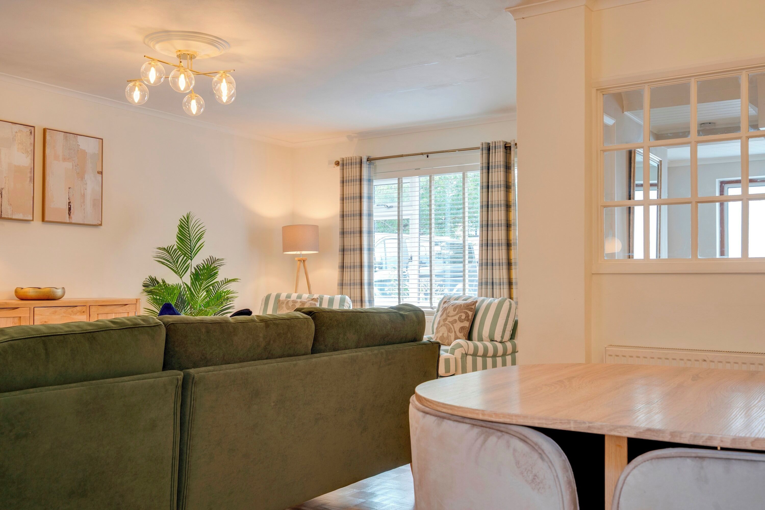 A living room with a green sofa, a dining table, and a window with curtains.