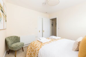 A hotel room with a bed, a chair, a radiator, and a door. - Stylish TownCentre Apartment|King Bed|Cotswold Way - Pass the Keys (Dursley)