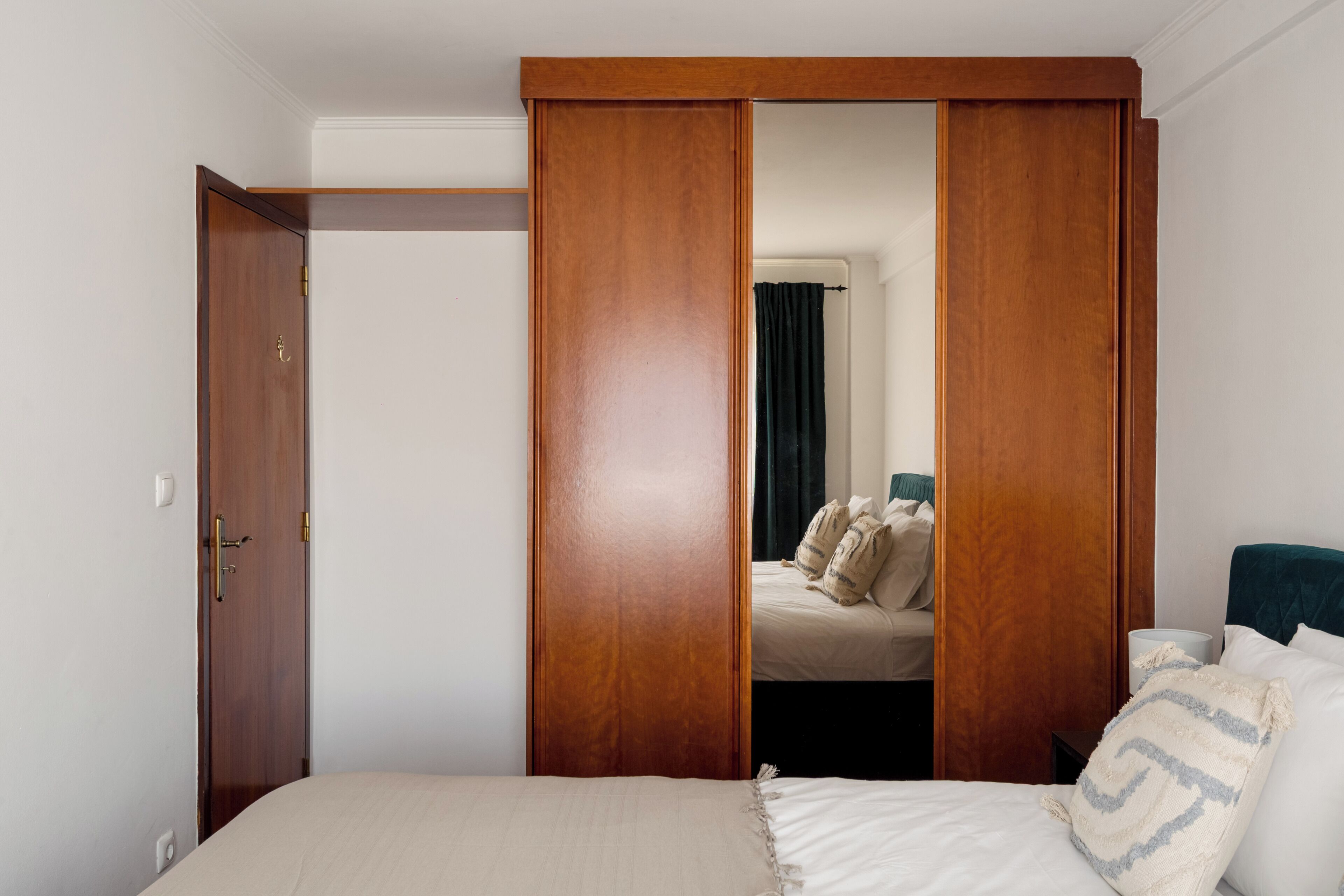 Une chambre à coucher avec un lit, une armoire en bois et un miroir qui reflète un lit avec des oreillers.