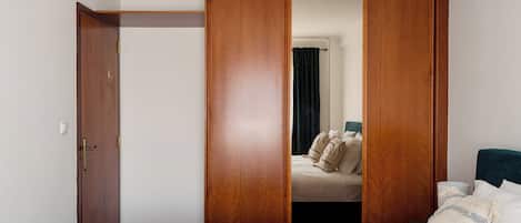Un dormitorio con una cama, un armario de madera y un espejo que refleja una cama con almohadas.