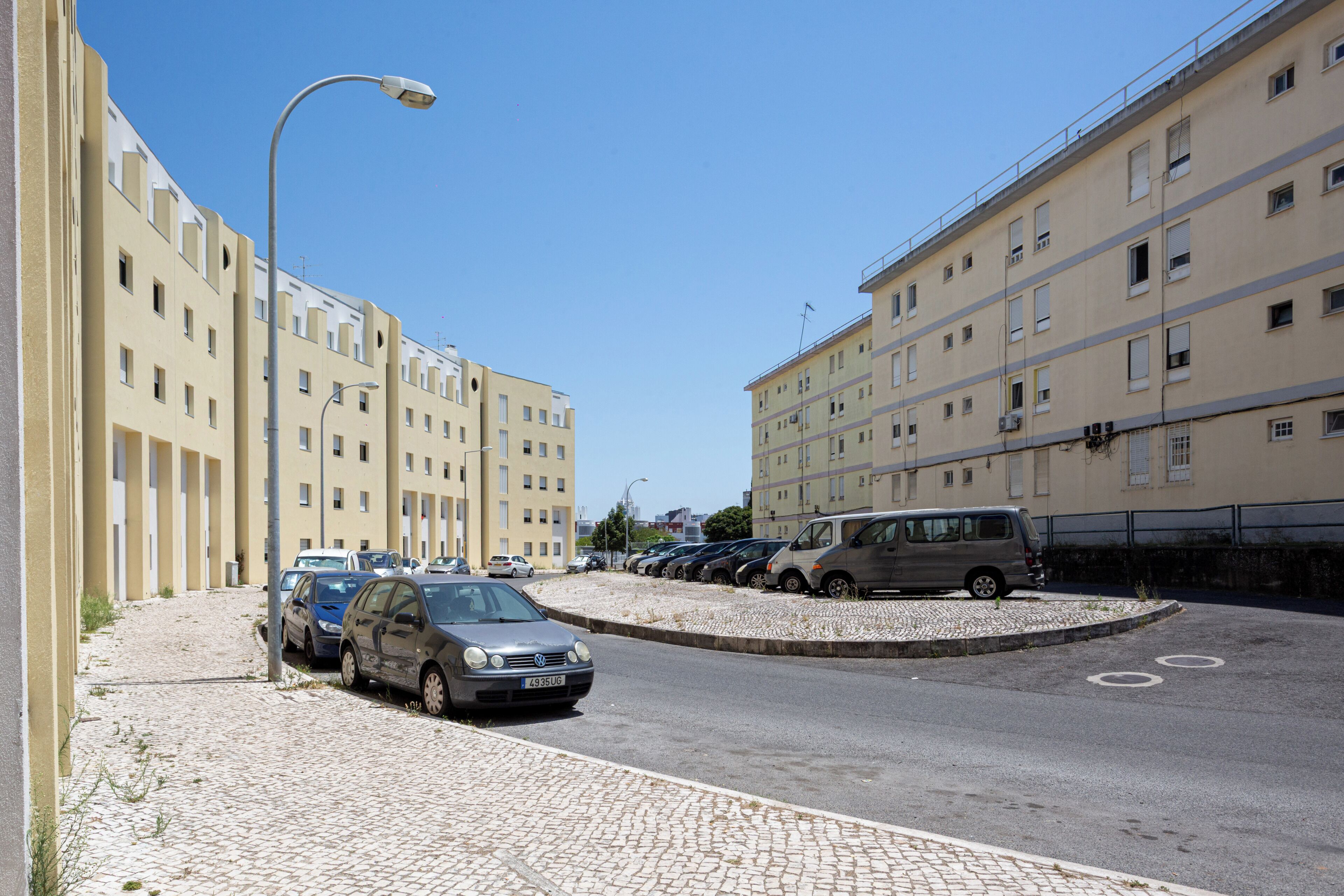 Ein Parkplatz mit mehreren Autos, einem Kopfsteinpflasterweg und einer Reihe von Gebäuden mit Balkonen.