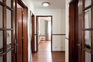 A hallway with wooden doors, a tiled floor, and a view into a bathroom with a shower and a toilet. - Lisbon Olivais Residence – 2BR Apartment (Lisbon)