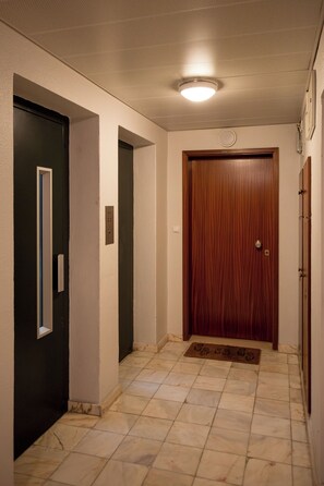 A hallway with a wooden door, a black door, and a light fixture on the ceiling. - Lisbon Olivais Residence – 2BR Apartment (Lisbon)