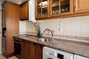 A kitchen with wooden cabinets, a stainless steel sink, a Bosch washing machine, and a water heater. - Lisbon Olivais Residence – 2BR Apartment (Lisbon)