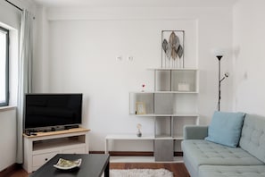Ein modernes Wohnzimmer mit Flachbildfernseher, einem grauen Sofa, einem weißen Couchtisch und einer weißen Stehlampe.