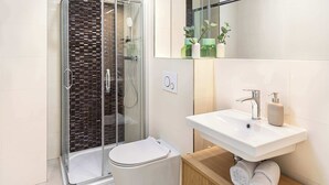 Ett modernt badrum med en duschavdelning med glasväggar, en vit toalett och ett badrumsskåp i trä med en tvättställ och förvaringsutrymme för handdukar.