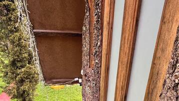 Eine Holztür mit einer strukturierten Wand, eine kleine Holztreppe zu einer Rasenfläche und ein Baum zur Linke.