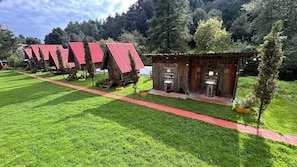 Une rangée de cabanes en bois aux toits rouges, un petit bâtiment en bois servant de toilettes avec un lavabo, et un chemin rouge.