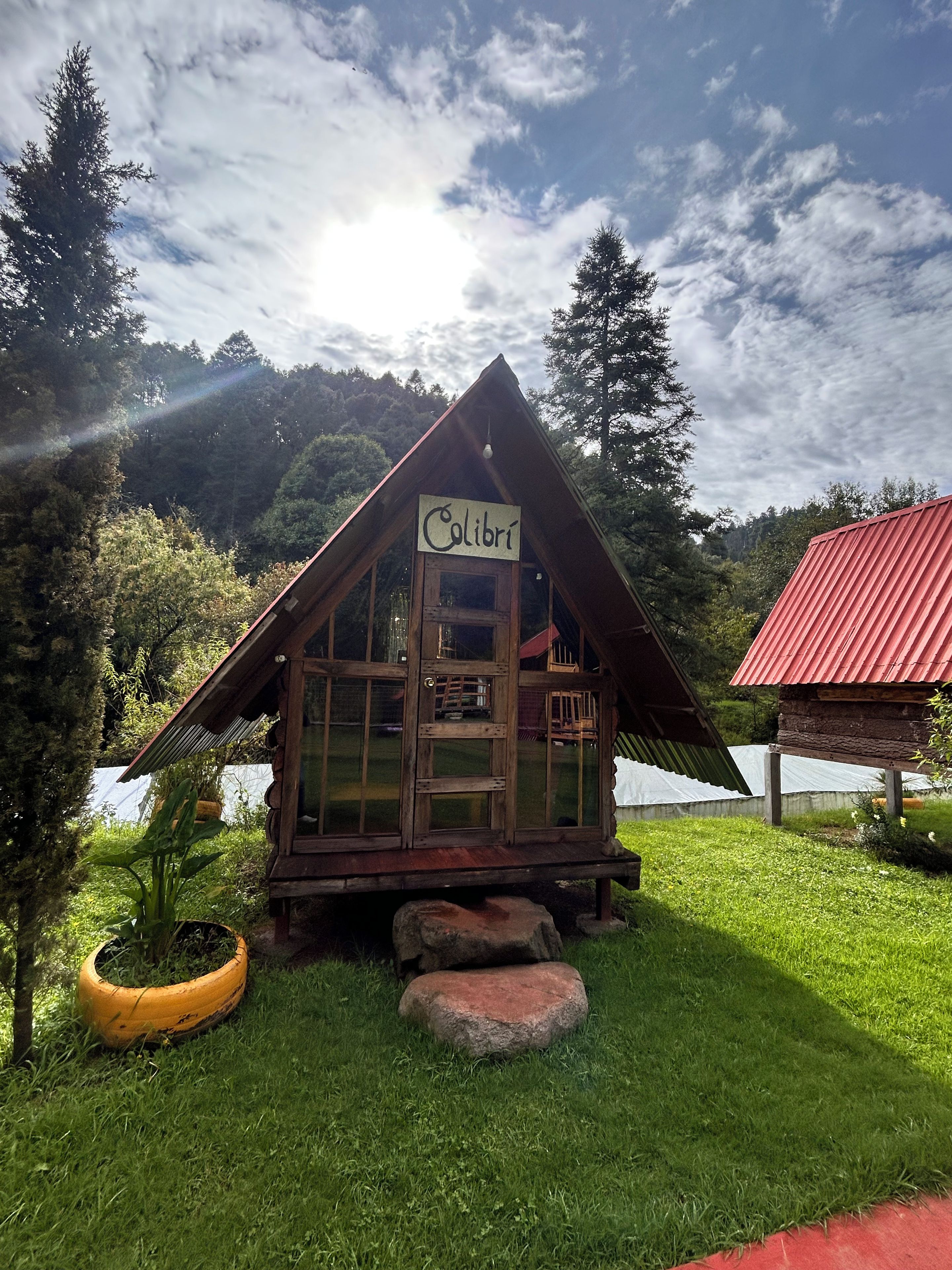 Una cabaña de madera con un letrero que dice 'Colibrí' en un entorno natural exuberante y verde.