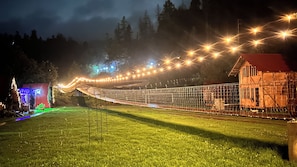 Un pont suspendu illuminé, un bâtiment avec un toit rouge et une zone herbeuse.