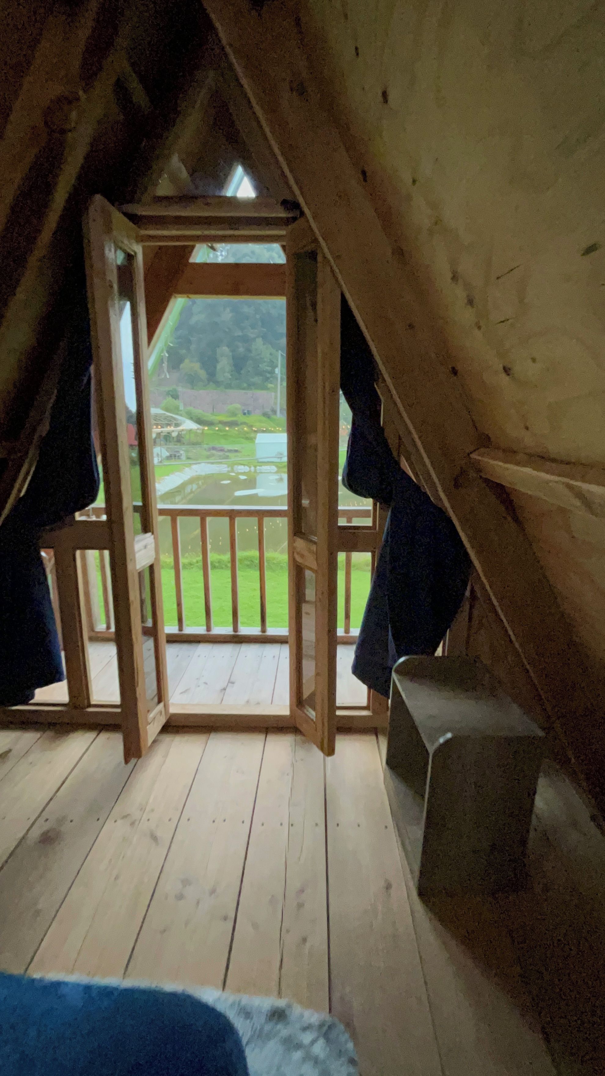 An attic room with a wooden floor, a small wooden bench, and a view of a green landscape through a doorway.