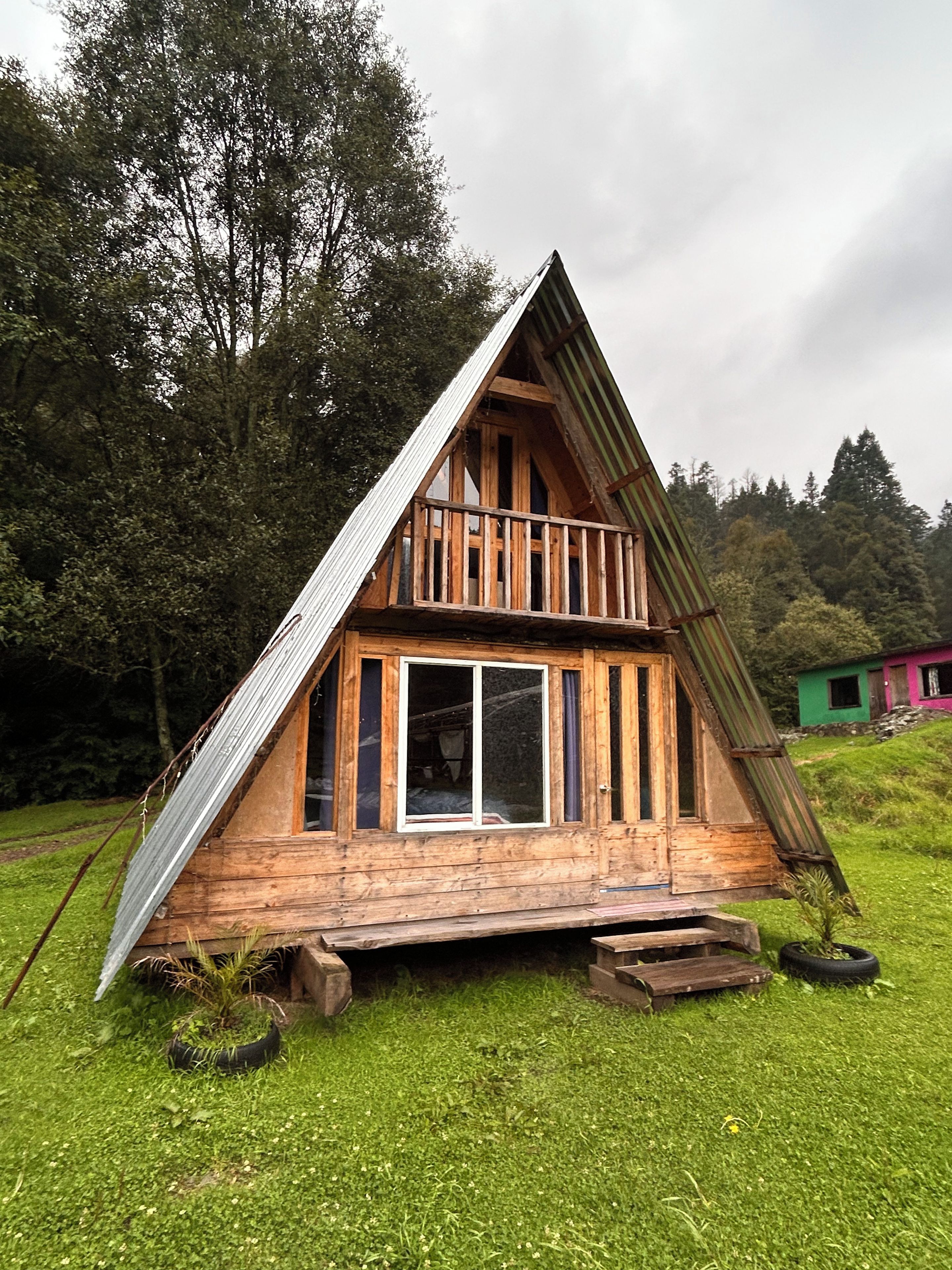 Una cabaña de madera con techo inclinado, un balcón y una ventana.