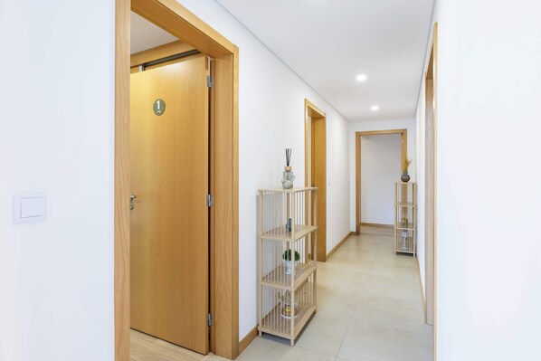 A hallway with wooden doors, a tiled floor, and a shelving unit with decorative items.