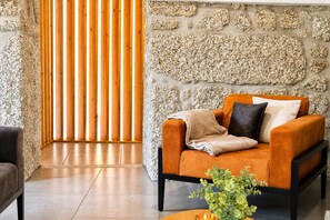 A modern living room with a stone wall, a wooden slatted partition, and a comfortable orange sofa with a throw blanket.