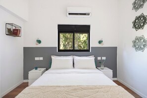 A bedroom with a bed, nightstands, an air conditioner, a window, and decorative wall art. - Modern City Apt Near Talpiot Market (Haifa)
