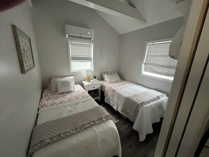 A bedroom with two single beds, a bedside table with a lamp, and a window with blinds. - Couples Escape w/ Hot Tub & Fire Pit Near the Lake (Clarklake)