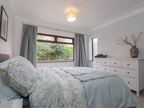 Ein Schlafzimmer mit einem Bett, einer Kommode, einem Fenster mit Vorhängen und einer Vase mit Zweigen.