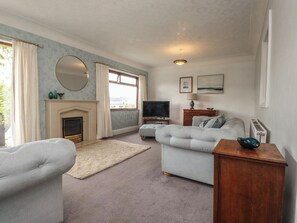 A living room with a fireplace, a television, a sofa, and a wooden side table. - Nampara (Colwyn Bay)