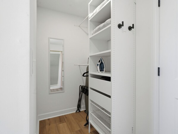 Ein weißer Kleiderschrank mit Regalen und Ablageflächen, ein Duschbereich mit Glasabtrennung und ein Holzboden.