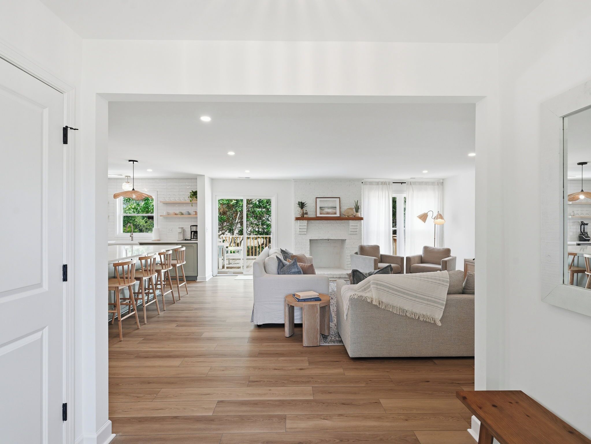 A spacious living area with a sofa, a coffee table, and a fireplace. There is a kitchen visible in the background with a dining area.