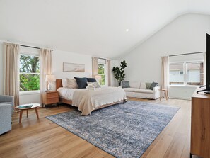 Ein Schlafzimmer mit einem Bett, Nachttischen, einer Couch, einem Schreibtisch und einem großen Fenster.