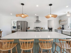 A modern kitchen with a large island, stainless steel appliances, and wooden chairs. - Sunny Days - Access The Masonboro Sound (Wilmington)