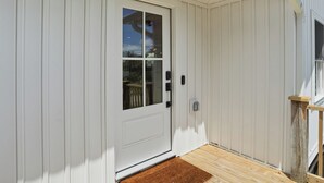 En vit dörr med ett glasparti, en liten veranda med ett träräcke och en brun dörrmatta.