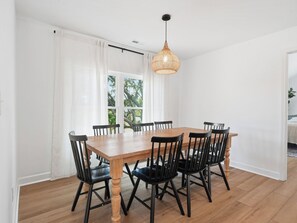 Ein Essbereich mit einem Holztisch, schwarzen Stühlen, einer gewobenen Pendelleuchte und Blick auf Bäume durch ein Fenster.