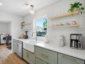 A modern kitchen with a built-in dishwasher, a coffee maker, and a window with a view of the outside. - Sunny Days - Access The Masonboro Sound (Wilmington)