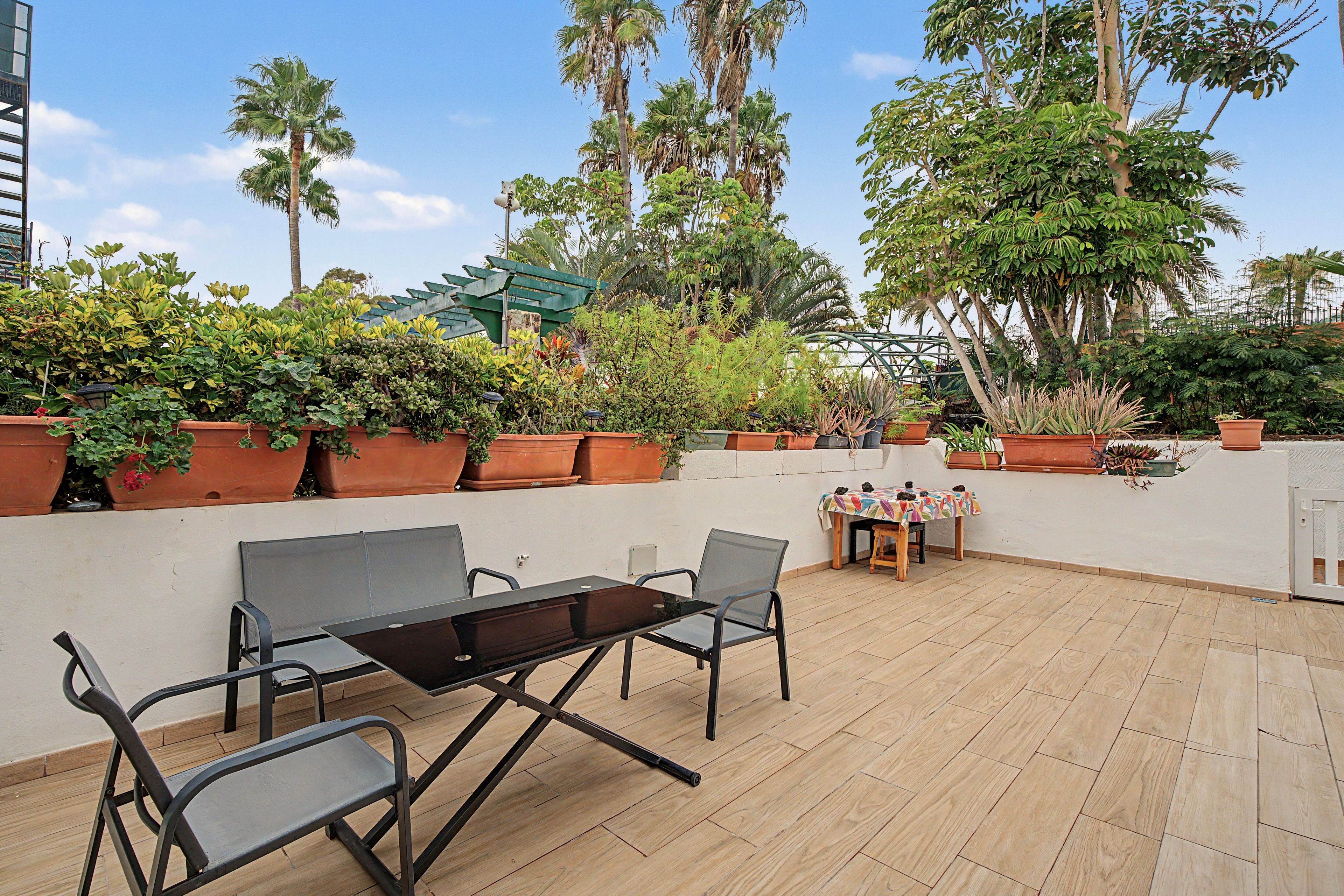 An outdoor patio with a table and chairs, surrounded by potted plants and trees.