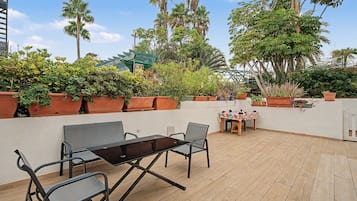 An outdoor patio with a table and chairs, surrounded by potted plants and trees.