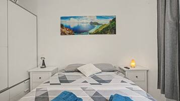 A bedroom with a bed, two bedside tables, a night lamp, a heater, and a painting of a landscape.