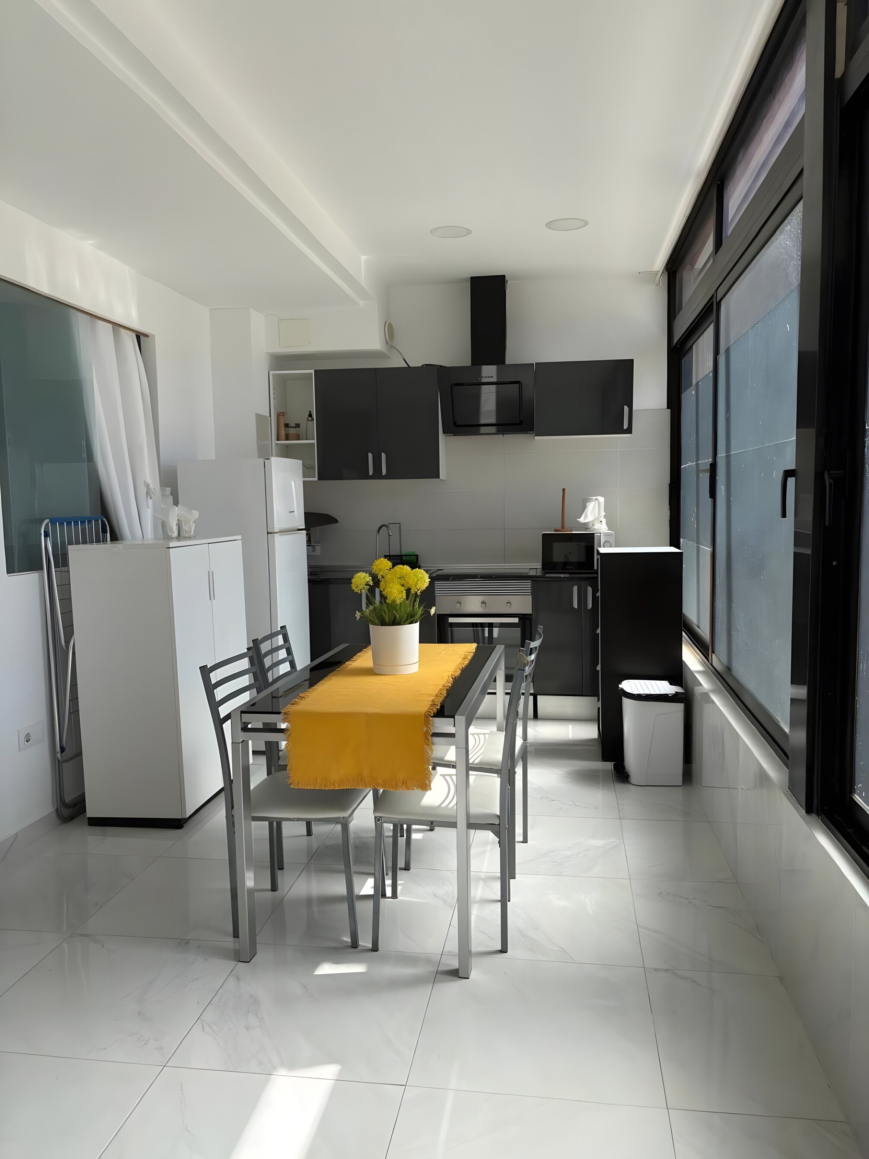 Una cocina moderna con comedor, armarios blancos, horno empotrado y ventana con vistas.