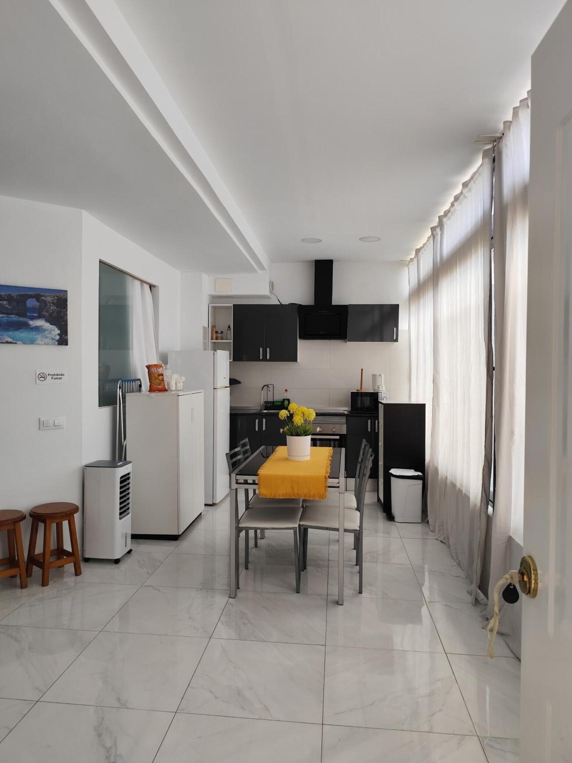 A modern kitchen with black cabinets, a white refrigerator, and a dining area with a yellow tablecloth.