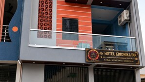 Um hotel de vários andares com uma placa chamativa para 'HOTEL KRIDHIKA INN' e uma entrada com portão.