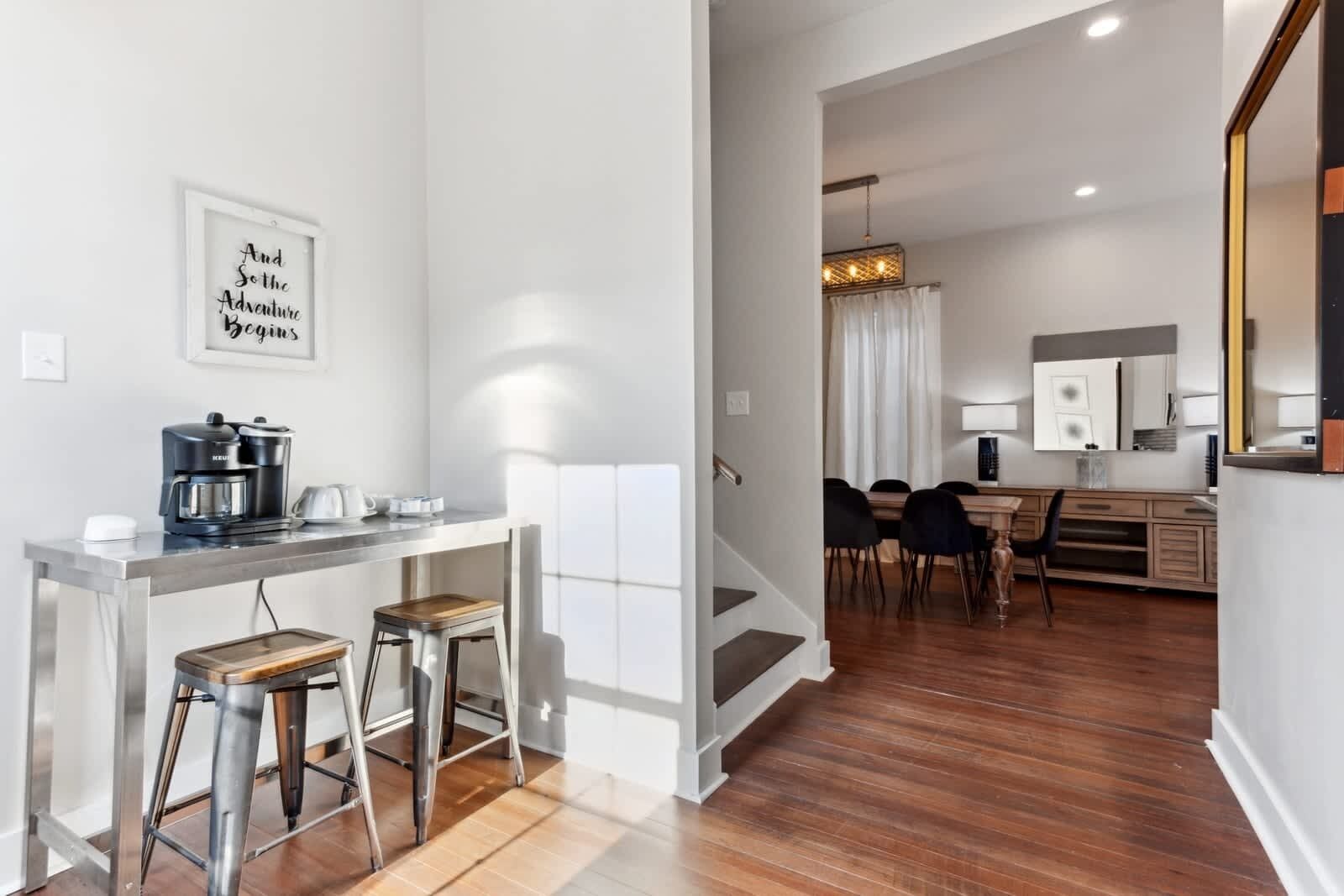 A modern kitchen with a coffee maker, bar stools, and a dining area with a table and chairs.