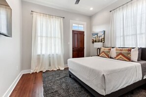 A bedroom with a bed, curtains, a door, and a painting on the wall. - Cozy Historic Home 5 Bedrooms Centrally Located (New Orleans)