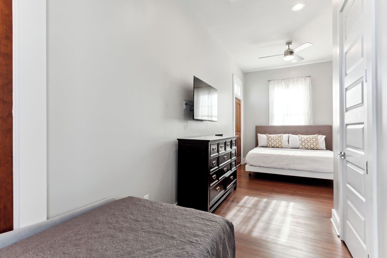 A bedroom with a bed, a dresser, a television, and a ceiling fan.