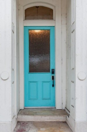 A turquoise door with a glass panel, a small step leading up to it, and a white wall with a circular window above. - LaBranche Pharmacy | Step Back in Time in a Historic Tremé Landmark- Walk to French Quarter (New Orleans)