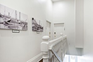 A hallway with white walls, a white railing, and black-and-white photographs on the wall. - LaBranche Pharmacy | Step Back in Time in a Historic Tremé Landmark- Walk to French Quarter (New Orleans)