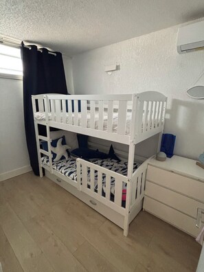 Ein Stockbett mit einer unteren Liege, eine Kommode mit Spiegel und ein Fenster mit Vorhängen.
